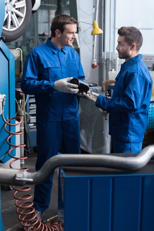 Professional pleasant mechanics talking and holding tools while repairing car