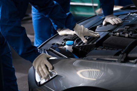 Professional mechanics examining engine while opening car bonnet