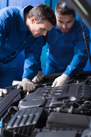 Concentrated experienced, mechanics talking and discussing break out while repairing car engineの写真素材