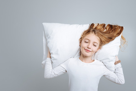Positive cute little girl lying on the pillow and smiling while pretending o sleepの写真素材