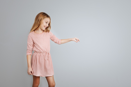 Pleasant pretty little girl holding hand aside while standing isolated on grey backgroundの写真素材