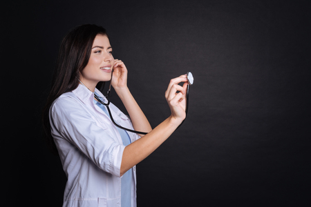 Positive professional female doctor holding stethoscope and examining her patient while being involved in work.の写真素材
