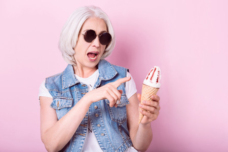 My favorite icecream. Expressive senior pretty woman opening her mouth and pointing on icecrem in...