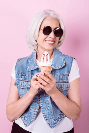 new taste. Senior positive pretty woman holding an icecream and smiling while standing against isolated pink background.の写真素材
