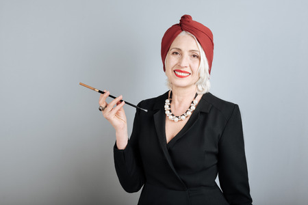 Like a star. Positive happy senior woman smiling and holding cigarette while standing against...