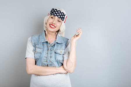 Great song. Joyful senior pretty woman smiling and listening to music while standing against isolated gray background.の写真素材