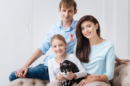Member of the family. Positive pretty joyful girl holding a cat and smiling while being with her familyの写真素材