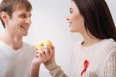 Tasty fruit. Happy delighted young couple looking at each other and smiling while holding an appleの写真素材