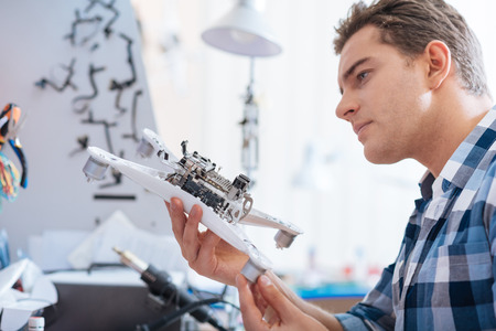 Test it. Concentrated young handsome man holding drone detail while discovering it and working as a repairman.の写真素材