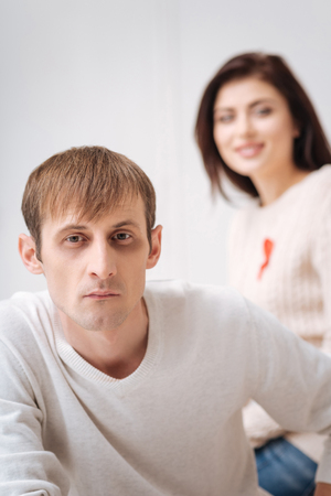 AIDS awareness. Thoughtful young serious man sitting in front of his girlfriend and looking at you while being supported by herの写真素材