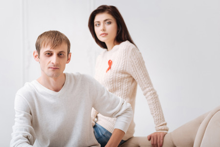 Be healthy. Handsome nice serious man sitting on the sofa and looking at you while being with his girlfriendの写真素材