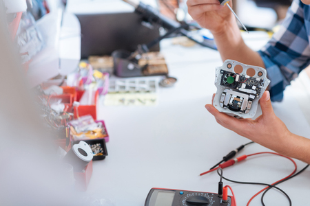 Hard but necessary. Close up of young man repairing drones chip and holding a screwdriver while using electronic tester.の写真素材