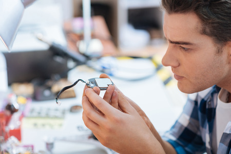 Keep it under control. Handsome serious young man discovering a chip of drone while repairing it and...