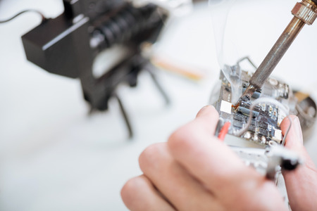 Near work. Close up of mans hands holding drone chip and using soldering iron while repairing it.