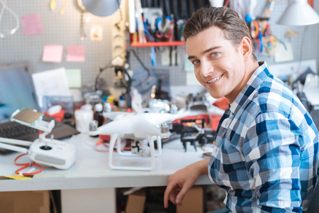 Smart and creative. Portrait of young handsome delighted man working with drone while sitting in the...