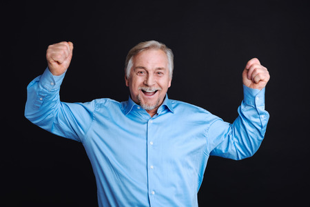 Feeling happiness. Grey-haired man expressing positivity holding both hands in air while standing...