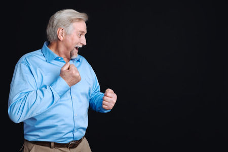 Keep fit. Positive delighted pensioner standing sideways with opened mouth wearing smart clothes keeping hands upの写真素材