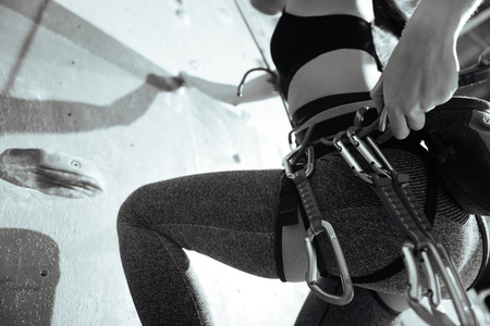 Conceptual and moving. Close up of slim young active woman climbing up the wall in gym while training and wearing sportswear and special equipmentの写真素材