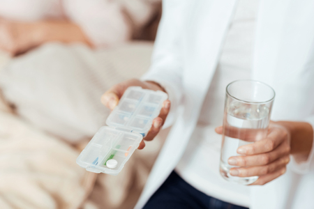 Take care of your health. Close up of pills in hands of professioanl caring nurse holding them and keeping glass of waterの写真素材