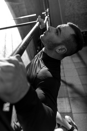 Pull up exercises. Serious well built handsome man holding a horizontal bar and doing pull ups while having an intensive workoutの写真素材