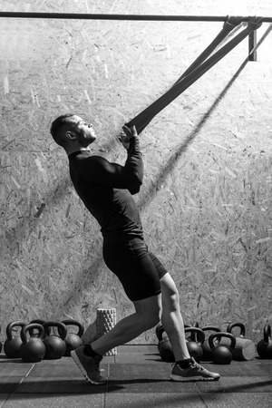 Building up muscles. Strong serious professional sportsman holding a resistance band and pulling it on him while developing his musclesの写真素材