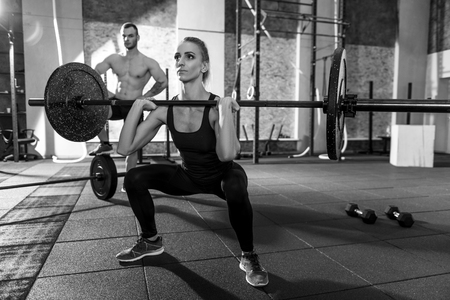 Powerlifting training. Strong well built beautiful woman squatting and holding a barbell while lifting itの写真素材