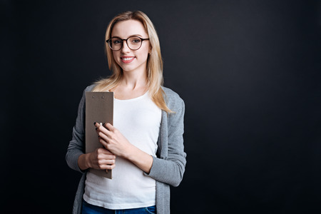 Like such way of life. Pleasant smiling young businesswoman holding folder and looking at you while expressing joyの写真素材