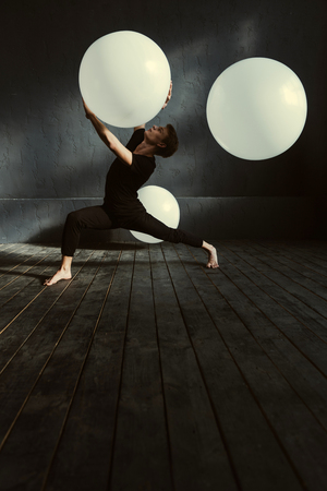 Performing with decoration. Expressive concentrated young dancer demonstrating his talent and expressing confidence while holding white balloon in the dark lighted studioの写真素材