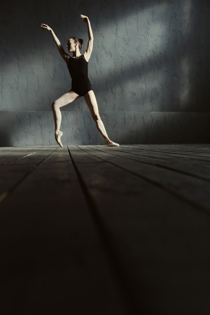 Full of inspiration. Involved flexible talented ballet dancer demonstrating her flexibility and expressing concentration while dancing in the black colored studio and standing on the tiptoeの写真素材