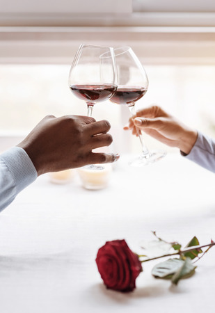 Our privacy. Positive peaceful delighted African American couple sitting in the restaurant and looking at each other while expressing affection and holding wineglassesの写真素材