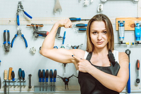Confident woman demonstrating her biceps in the workshopの写真素材