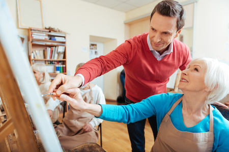Smiling artist helping elderly woman in painting studioの写真素材