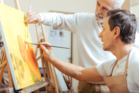 Elderly artist painting with his young colleague.の写真素材