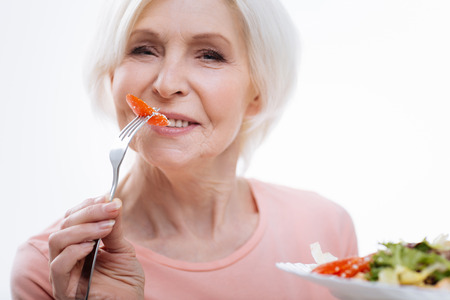 Portrait of aged female while eating tomatoの写真素材