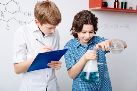 Thoughtful smart boy noting down results of the experimentの写真素材