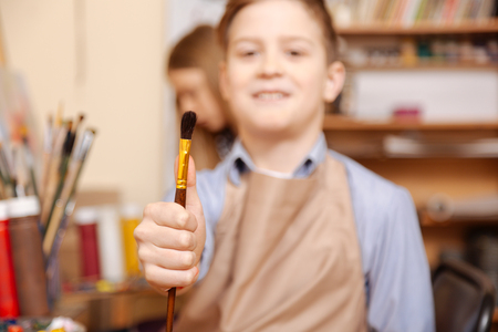 Delighted little boy holding paintbrush at the art classの写真素材