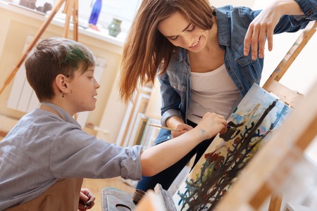 Helpful young woman teaching painting kid at school
