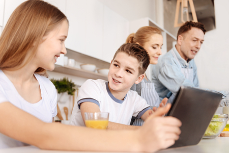 Cheerrful siblings sitting in the kitchen using tabletの写真素材