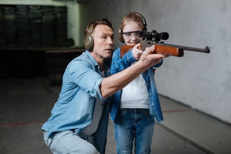 Happy delighted girl looking into the optical sight with guidance of her fatherの写真素材