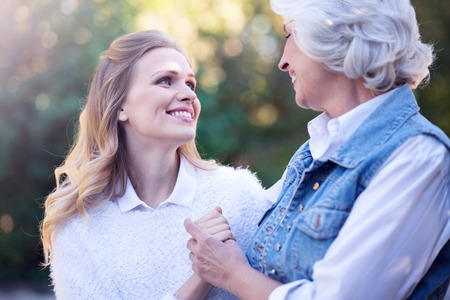 Smiling aging woman and mature daughter walking in the parkの写真素材