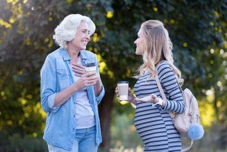Joyful pregnant woman enjoying conversation with aged mother outdoorsの写真素材