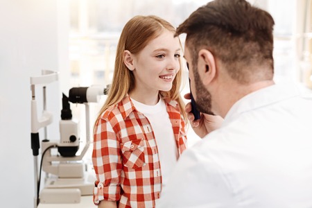 Competent cool doctor having a look at girls eyesの写真素材