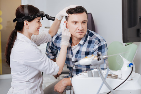 Happy young doctor examining ear of her friendの写真素材