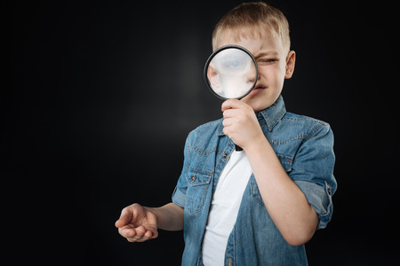 Handsome boy looking at camera through magnifierの写真素材