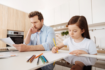 Girl drawing next to her working fatherの写真素材