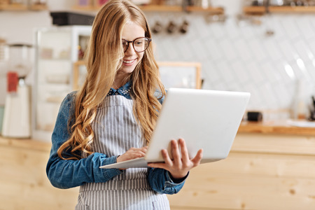Lovely young barista standing and holding a laptopの写真素材