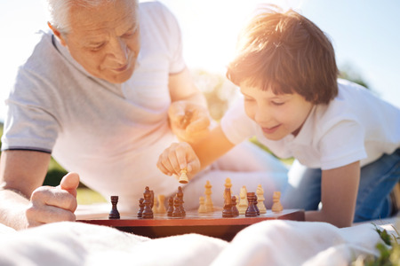 Wise nice man encouraging his grandchild playing chess