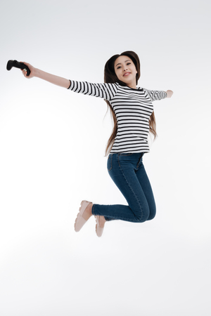 Joyful girl stretching arms while jumping highの写真素材