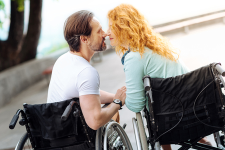Pleasant senior wheelchaired couple sitting nose to noseの写真素材