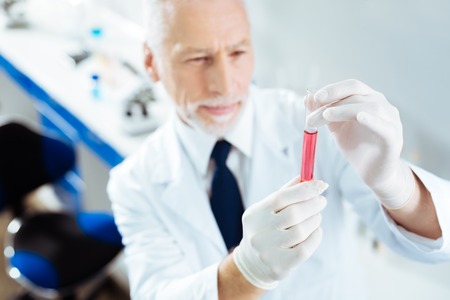 Concentrated elderly man examining pink liquidの写真素材